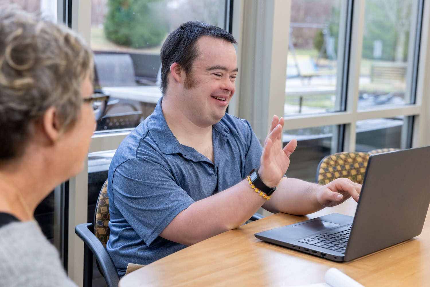 Eine Person grüßt jemandem am Computer während jemand anderes dabei sitzt.